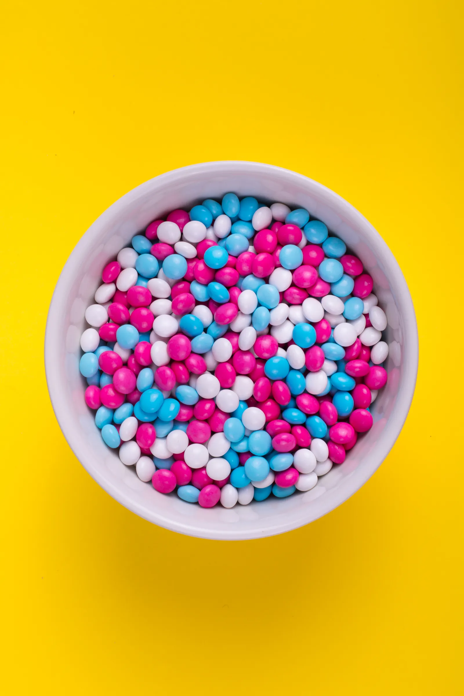 Bunte Schokolinsen in einer weißen Schale auf gelbem Hintergrund - **Dateiname**: bonbons-schale-bunt.webp - **Platzierung**: Nach der H3-Überschrift „Süßigkeiten: Der Sympathieträger"