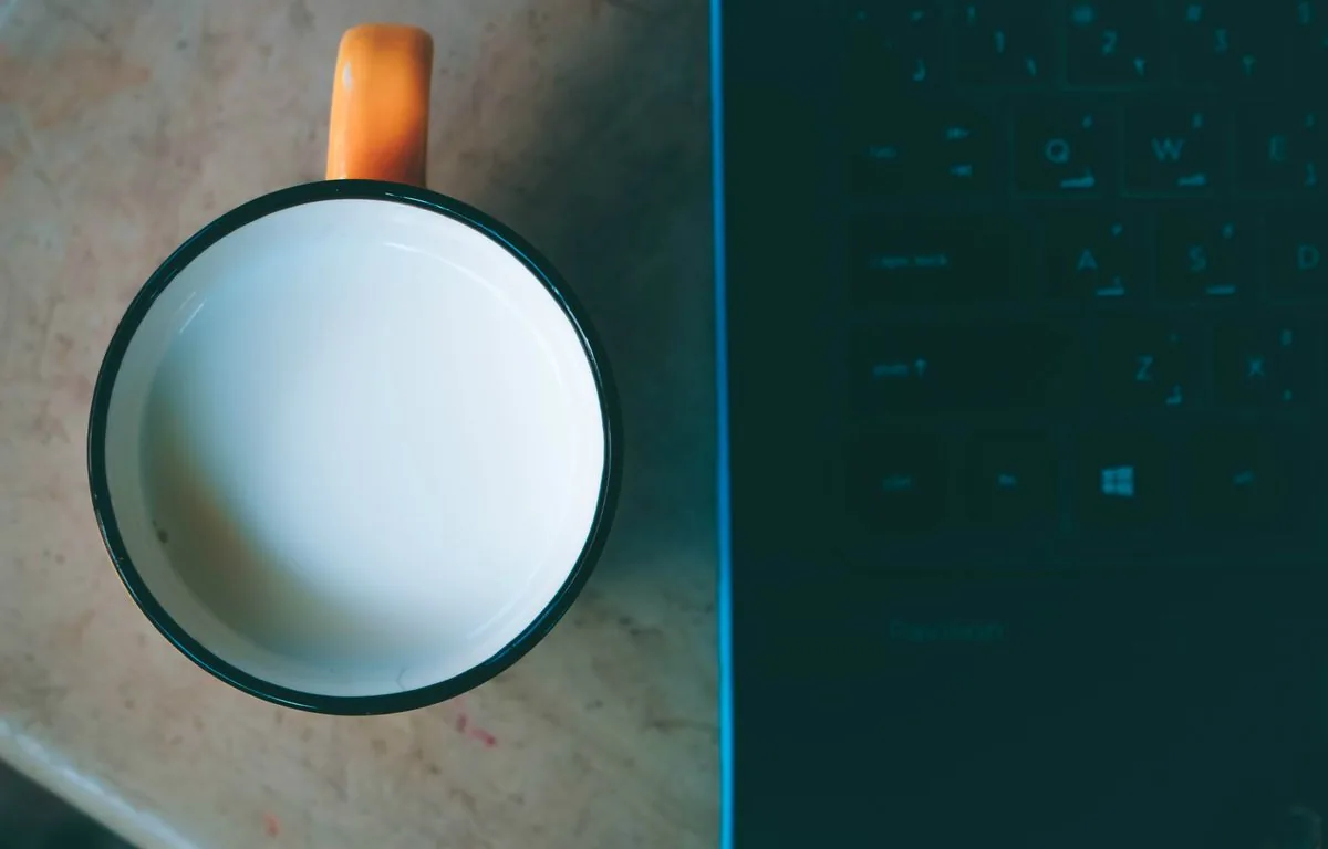 Weiße Tasse von oben neben einem Laptop auf einem Schreibtisch