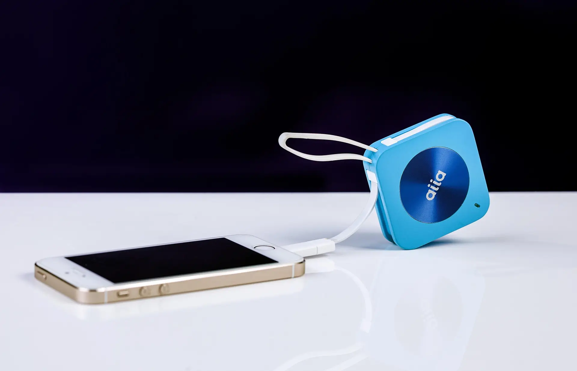 Blauer Powerbank Werbeartikel mit Logo liegt neben einem Smartphone und ist per Ladekabel verbunden