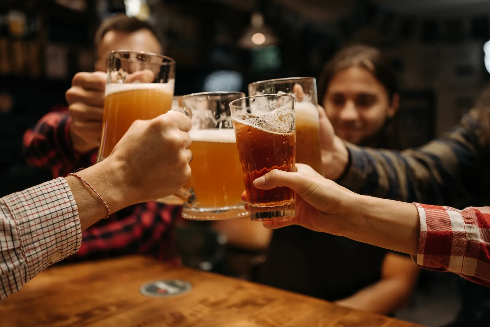 Freunde stoßen an einem Holztisch mit gefüllten Biergläsern an