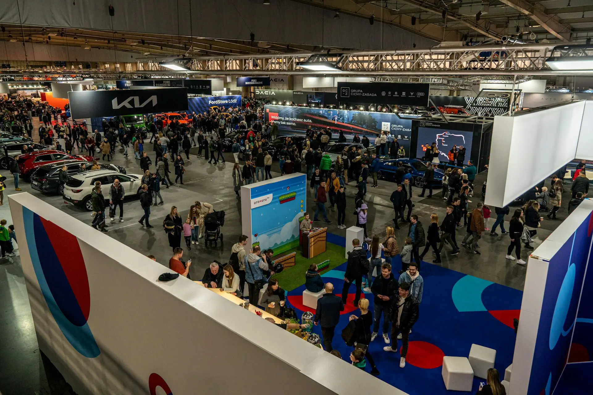 Blick von oben in eine große Messehalle mit vielen Besuchern, Messeständen und ausgestellten Autos bei einem Event