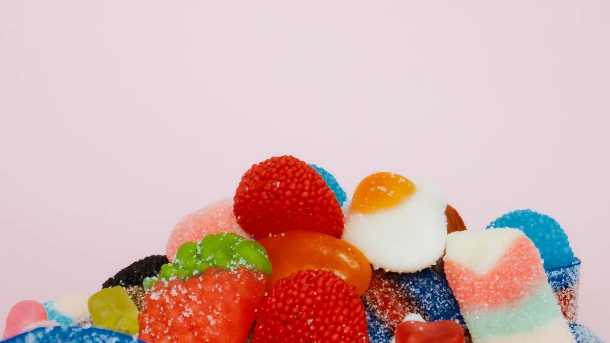 Bunter Haufen zuckriger Fruchtgummis in verschiedenen Formen vor rosa Hintergrund
