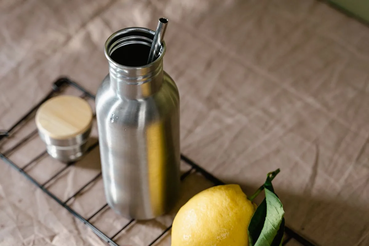 Silberne Edelstahl-Trinkflasche mit Metallhalm neben einer Zitrone